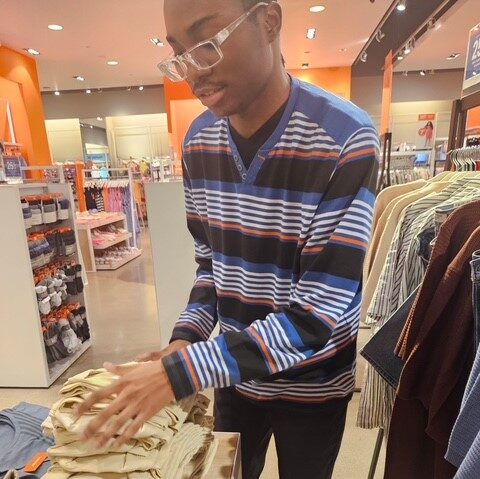 A young man in a striped sweater stacking clothes in a retail store.